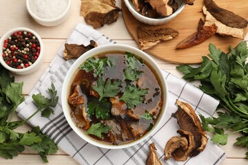 Tasty soup with mushrooms and parsley in bowl on light wooden table, flat lay