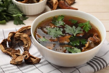 Tasty soup with mushrooms and parsley in bowl on light wooden table, closeup