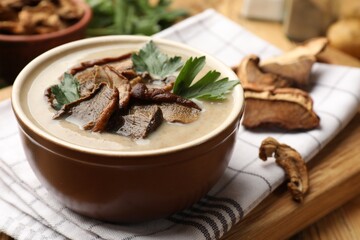 Tasty cream soup with mushrooms and parsley in bowl on wooden table, closeup