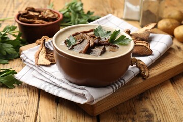 Tasty cream soup with mushrooms and parsley in bowl on wooden table, closeup