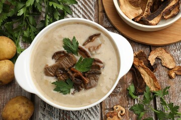 Tasty cream soup with mushrooms and parsley in bowl on color wooden table, flat lay