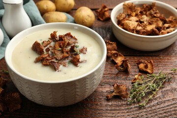 Tasty cream soup with mushrooms and thyme in bowl on wooden table, closeup
