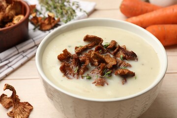 Tasty cream soup with mushrooms and thyme in bowl on light wooden table, closeup
