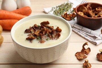 Tasty cream soup with mushrooms and thyme in bowl on light wooden table, closeup