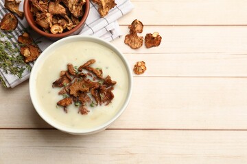 Tasty cream soup, thyme and dry chanterelle mushrooms on light wooden table, flat lay. Space for text