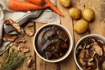 Tasty soup with mushrooms in bowl and products on wooden table, flat lay