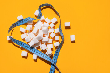 White sugar cubes and measuring tape on yellow background flat lay top view. Concept of sweets consumption and addiction, global health and excess weight issue, sugar-free diet, sports and fitness
