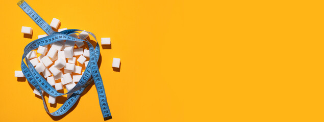 White sugar cubes and measuring tape on yellow background flat lay top view. Concept of sweets...