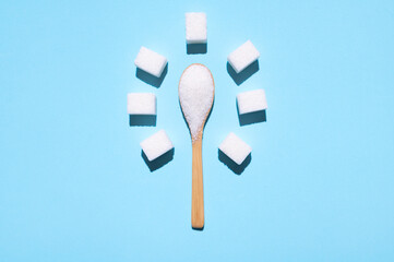 White granulated sugar in wooden spoon and sugar cubes on blue background. Concept of eating sweets, health and diabetes issue, sugar addiction, sugar-free diet. Top view flat lay