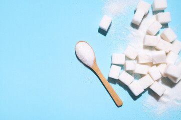 White granulated sugar in wooden spoon and sugar cubes on blue background. Concept of eating...