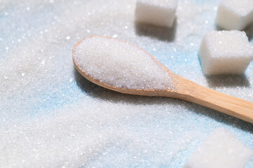 White granulated sugar in wooden spoon and sugar cubes on blue background. Concept of eating sweets, health and diabetes issue, sugar addiction, sugar-free diet. Top view flat lay