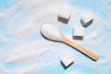 White granulated sugar in wooden spoon and sugar cubes on blue background. Concept of eating sweets, health and diabetes issue, sugar addiction, sugar-free diet. Top view flat lay