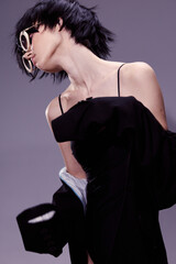 stylish woman with short black hair wearing sunglasses and black dress poses against minimalist...