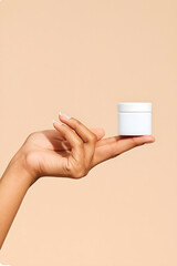 Graceful fingers present blank white jar on nude backdrop. Dedos elegantes muestran tarro. Doigts élégants montrent pot. Elegante Hand mit Tiegel.