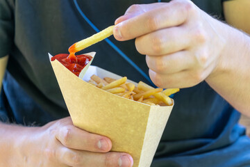 Male dipping french fries into ketchup outdoors