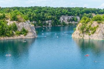 Tranquil lake with kayakers and lush green cliffs on a sunny day. Zakrzowek lagoon. Krakow