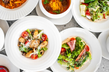 Top view of assorted gourmet dishes including pasta, soup, and salads with fresh ingredients, arranged on a table, ideal for food photography and culinary themes.