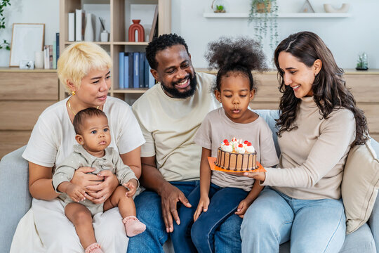 In a heartwarming celebration, Parents gather joyfully around their little daughter as she prepares to blow out the candles on her birthday cake, father and mother clapping happy at a milestone event - Powered by Adobe