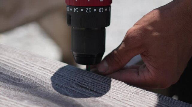 Drill Hand Screwing Man using power drill to screw into wooden deck plank close up