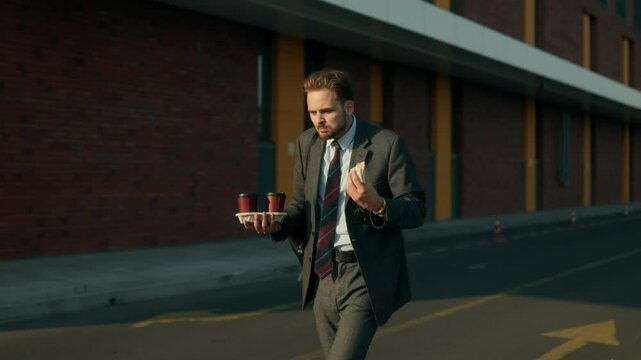 Young office man eating sandwich and rushing through city street