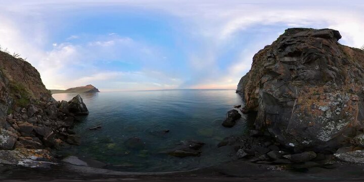 360 VR panoramic footage of the shore near a steep dark cliff Lake Baikal National Park, peaceful relaxing waves view of clean fresh blue water expanse, pre-sunset time golden hour, virtual immersive