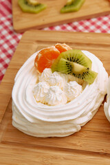 Delicious pavlova dessert with whipped cream mandarin kiwi on wooden board
