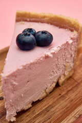 Delicious pink blueberry cheesecake slice on wooden plate with fresh fruit topping