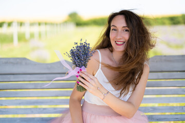 a beautiful girl in a dress with a bouquet of lavender flowers sits on a bench