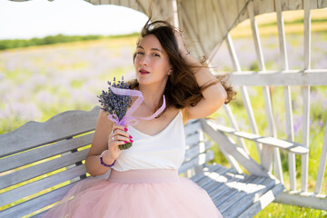 a beautiful girl in a dress with a bouquet of lavender flowers sits on a bench