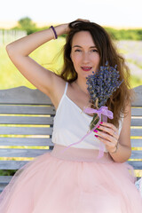 a beautiful girl in a dress with a bouquet of lavender flowers sits on a bench