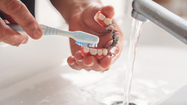Woman washing her dentures in running water - Powered by Adobe