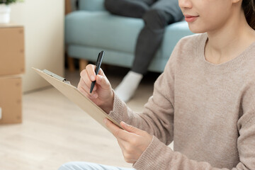 Move house, relocation. Woman using household checklist for new apartment Inside the room are...