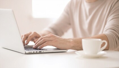 Fototapeta premium 温かみのある自然光に包まれたワークスペースで、白いコーヒーカップが置かれた木製デスクの上で、女性がシルバーのラップトップコンピューターを操作している様子。ベージュの長袖を着た手がキーボードの上に置かれ、集中して作業に取り組む穏やかで心地よい在宅勤務の風景