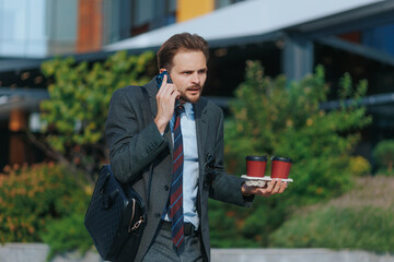 Business guy hustling downtown, coffee cups in hand, talking on phone