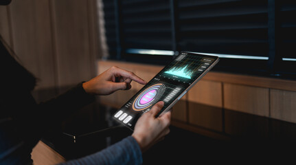 A person interacts with a transparent, futuristic tablet displaying data and graphs in a dimly lit,...