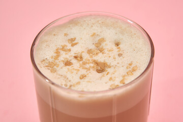Creamy walnut latte on pink surface with fresh foam and nut toppings in a glass cup