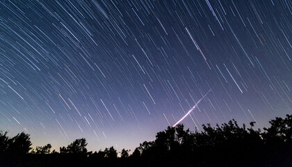 Bright jet trail arcs over military base under starlit sky, long exposure night shot