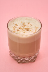 Creamy almond latte in clear glass on pink background with nut topping