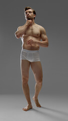 Studio male model posing in white underwear touching neck on gray background. Concept of fashion,...
