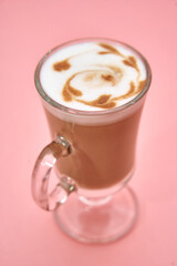 Elegant glass cup of cappuccino with swirl latte art on pink background