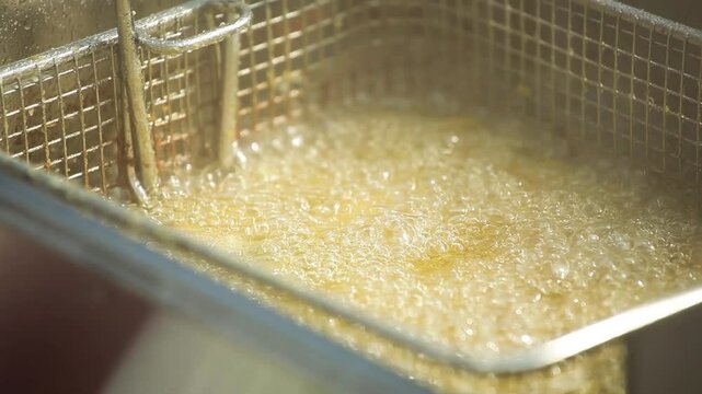 Close-up shot of street food fish being deep-fried in boiling oil using a metal wire basket. Hot bubbles rise as the crispy surface forms. Authentic urban cooking scene with sizzling sound and golden 