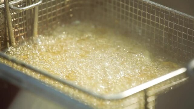 Close-up shot of street food fish being deep-fried in boiling oil using a metal wire basket. Hot bubbles rise as the crispy surface forms. Authentic urban cooking scene with sizzling sound and golden 