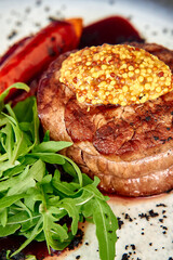 Grilled beef steak with mustard garnish and rocket leaves accompanied by red bell pepper
