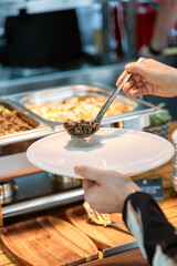 Buffet serving: hands scoop gourmet dish at food station with ladle over plate