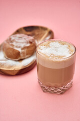 Powdered sugar donut and cappuccino on pink background with wooden plate