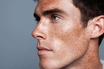 Obraz premium Close up side profile of young man with clear skin and subtle freckles, showing natural beauty and calm expression against plain gray background