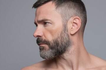 Fototapeta premium Man with short beard side profile close up, showing facial hair and serious expression on neutral gray background