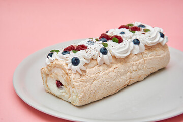 Delicious pavlova roulade with whipped cream and berries on plate against pink background