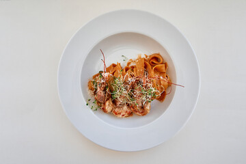 Gourmet pasta dish with microgreens and tomato sauce on white plate