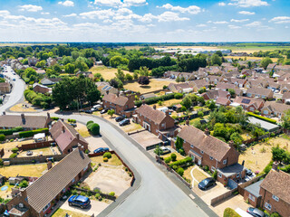 Aerial view if rows of semi detached houses and bungalows seen in drought conditions in England during summer 2025. A warehouse and storage facility can be seen in the distance.